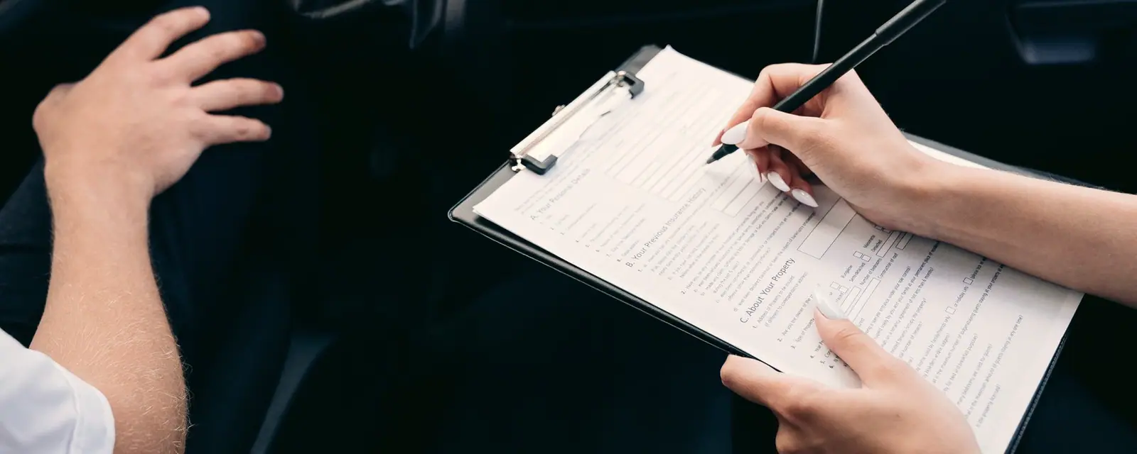A person filling out paperwork inside a car